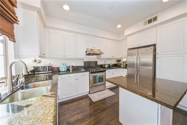 a kitchen with granite countertop a sink stainless steel appliances and white cabinets