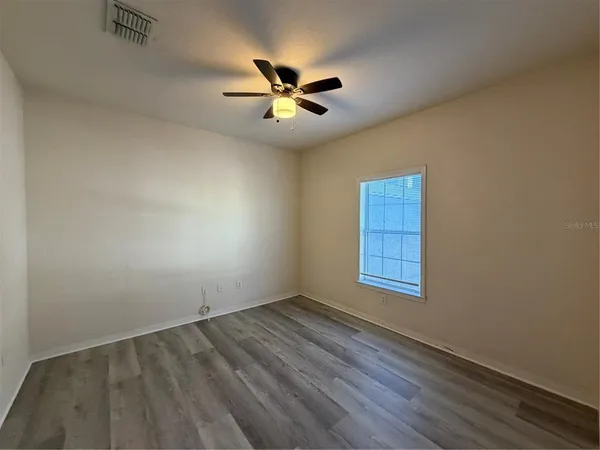 an empty room with wooden floor fan and windows