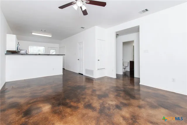 a view of an empty room with kitchen and a window