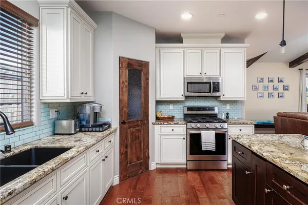 a kitchen with stainless steel appliances granite countertop a refrigerator a sink dishwasher a stove and white cabinets with wooden floor