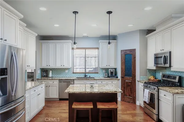 a kitchen with stainless steel appliances kitchen island granite countertop a refrigerator a stove a sink a dining table and chairs with wooden floor