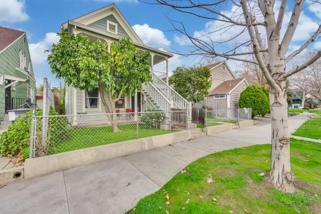 a view of a white house with a small yard and large tree