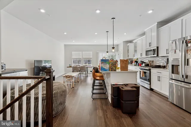 a kitchen with stainless steel appliances kitchen island granite countertop a stove top oven a sink a refrigerator and white cabinets with wooden floor