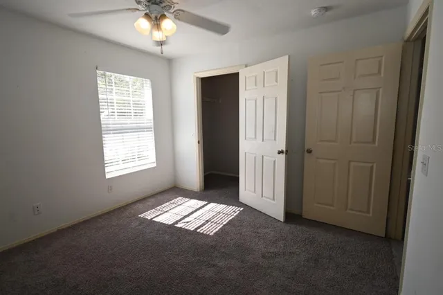 an empty room with chandelier fan and windows