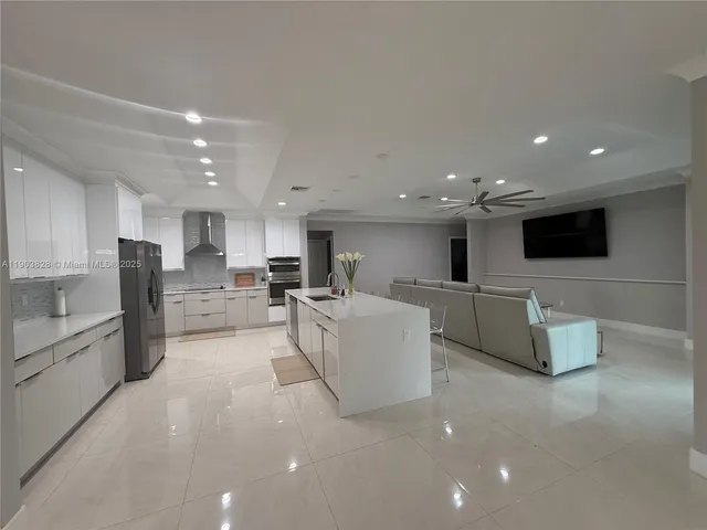 a large white kitchen with stainless steel appliances kitchen island a large counter top space and a couch