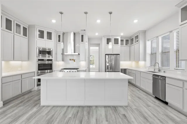 a large white kitchen with kitchen island a stove a sink dishwasher and white cabinets with wooden floor