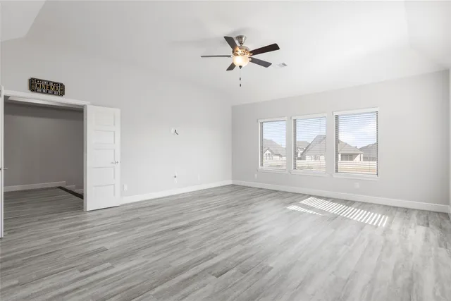an empty room with wooden floor fan and windows