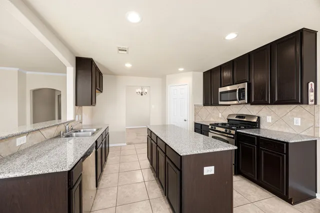 a kitchen with stainless steel appliances granite countertop a stove top oven a sink dishwasher and a refrigerator with wooden cabinets