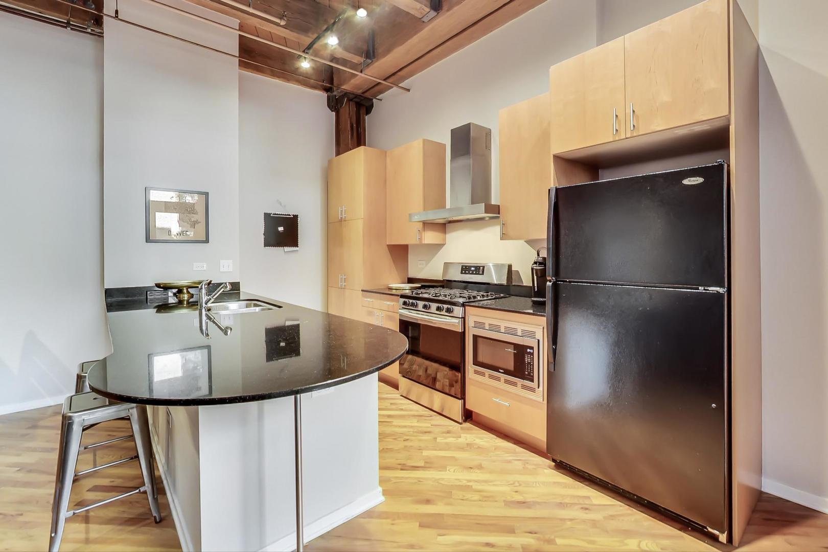 1040 West Adams Street, Unit 220 Chicago, IL 60607 - Photo 26 of 27 a kitchen with kitchen island a counter top space and stainless steel appliances