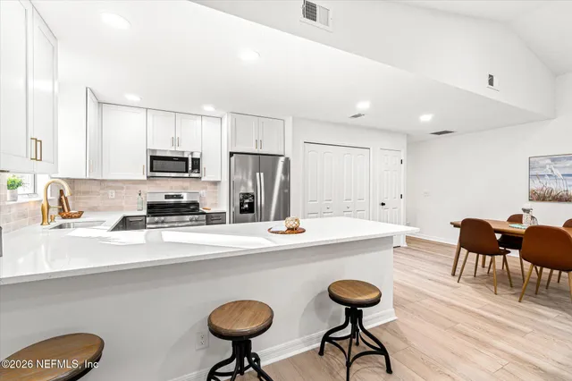 a kitchen with stainless steel appliances a dining table chairs refrigerator and sink