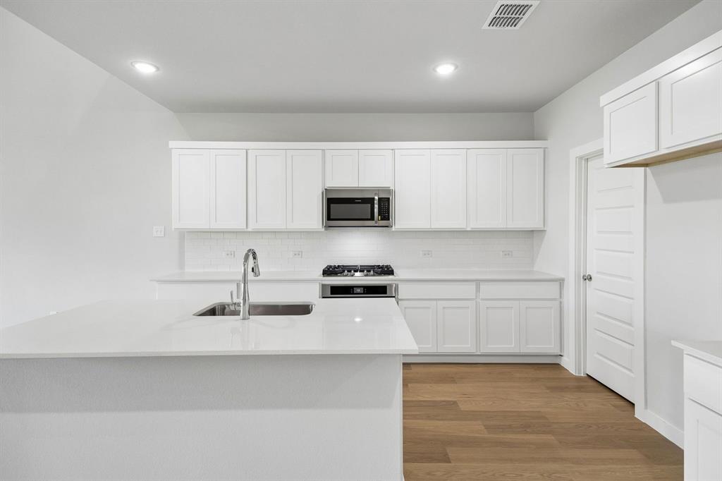 1460 Companero Street Haslet, TX 76052 - Photo 7 of 35 a kitchen with stainless steel appliances granite countertop a sink a stove a microwave a refrigerator a white cabinets and wooden floor