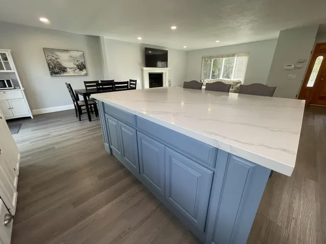 a view of a kitchen with kitchen island a counter top space a sink wooden floor and a large window