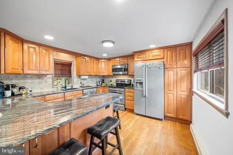 a kitchen with stainless steel appliances granite countertop a refrigerator a sink dishwasher a stove and a dining table with wooden floor