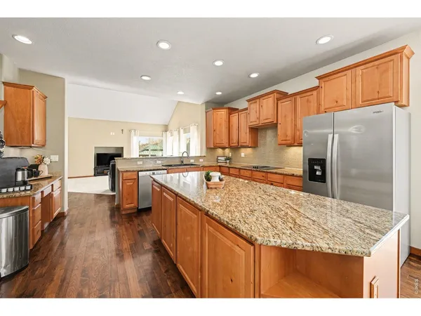 a kitchen with stainless steel appliances granite countertop a refrigerator a sink dishwasher a oven with white cabinets and wooden floor