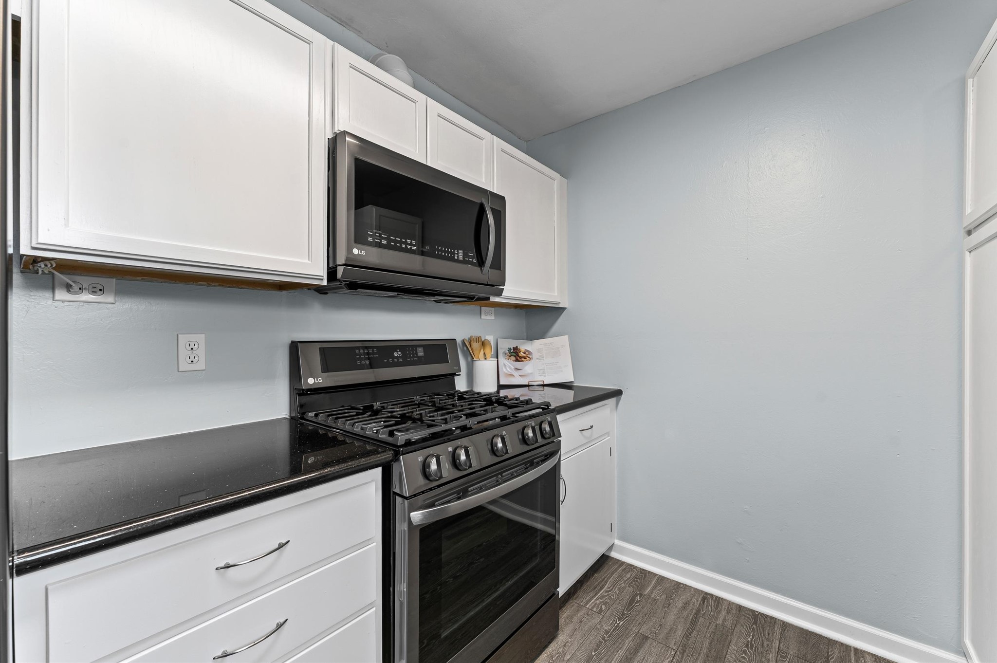 9810 Charter Ridge Drive Houston, TX 77070 - Photo 11 of 28 This kitchen features sleek black countertops, white cabinetry, and modern stainless steel appliances, including a gas range and overhead microwave. The soft gray walls and wood-look flooring create a fresh and inviting atmosphere.
