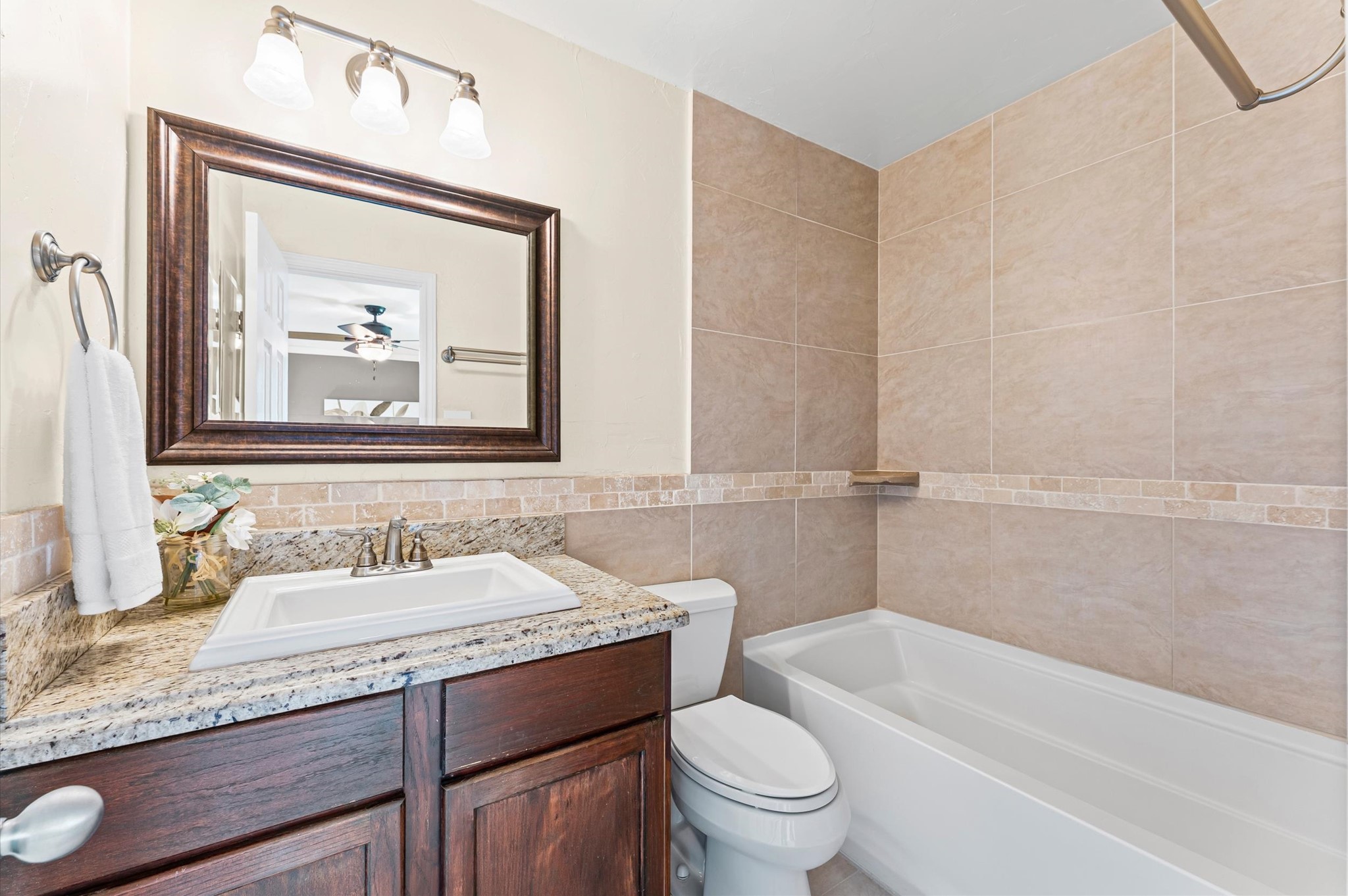 9810 Charter Ridge Drive Houston, TX 77070 - Photo 15 of 28 This bathroom features a modern design with beige tiled walls and a granite countertop. It includes a large mirror, elegant lighting, a bathtub, and a sleek vanity for a clean, contemporary look.