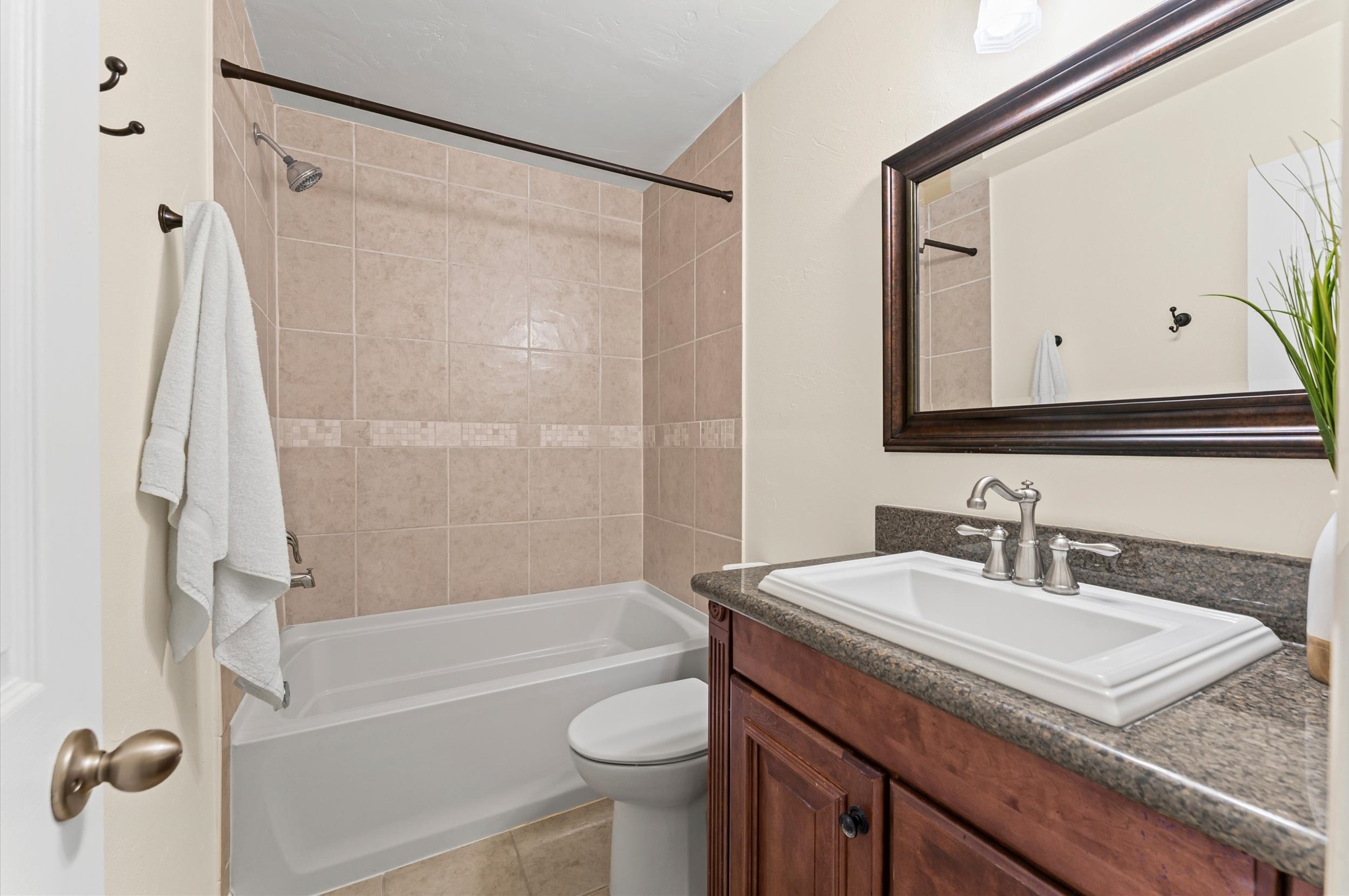 9810 Charter Ridge Drive Houston, TX 77070 - Photo 20 of 28 This clean, modern hall bathroom featuring a tiled shower-tub combo, a sleek vanity with a dark countertop, and a large framed mirror. It’s well-lit and has neutral tones, offering a warm and inviting atmosphere.