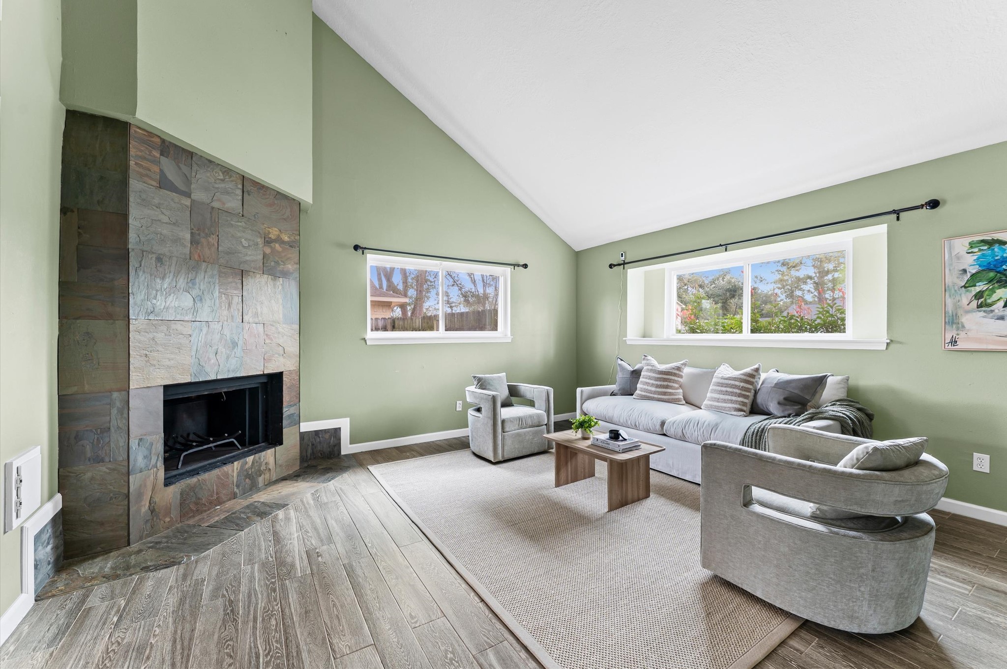 9810 Charter Ridge Drive Houston, TX 77070 - Photo 5 of 28 This spacious living room features high vaulted ceilings, a cozy stone fireplace, and large windows that allow natural light to fill the room. The soft green walls and modern furnishings create an inviting and comfortable atmosphere.