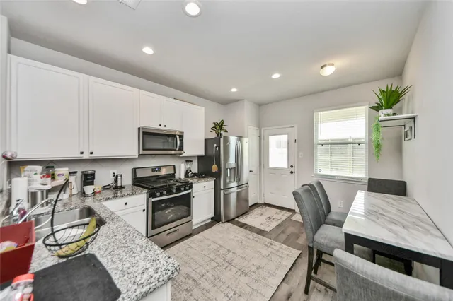 a kitchen with stainless steel appliances granite countertop a stove top oven a sink dishwasher a dining table and chairs with wooden floor