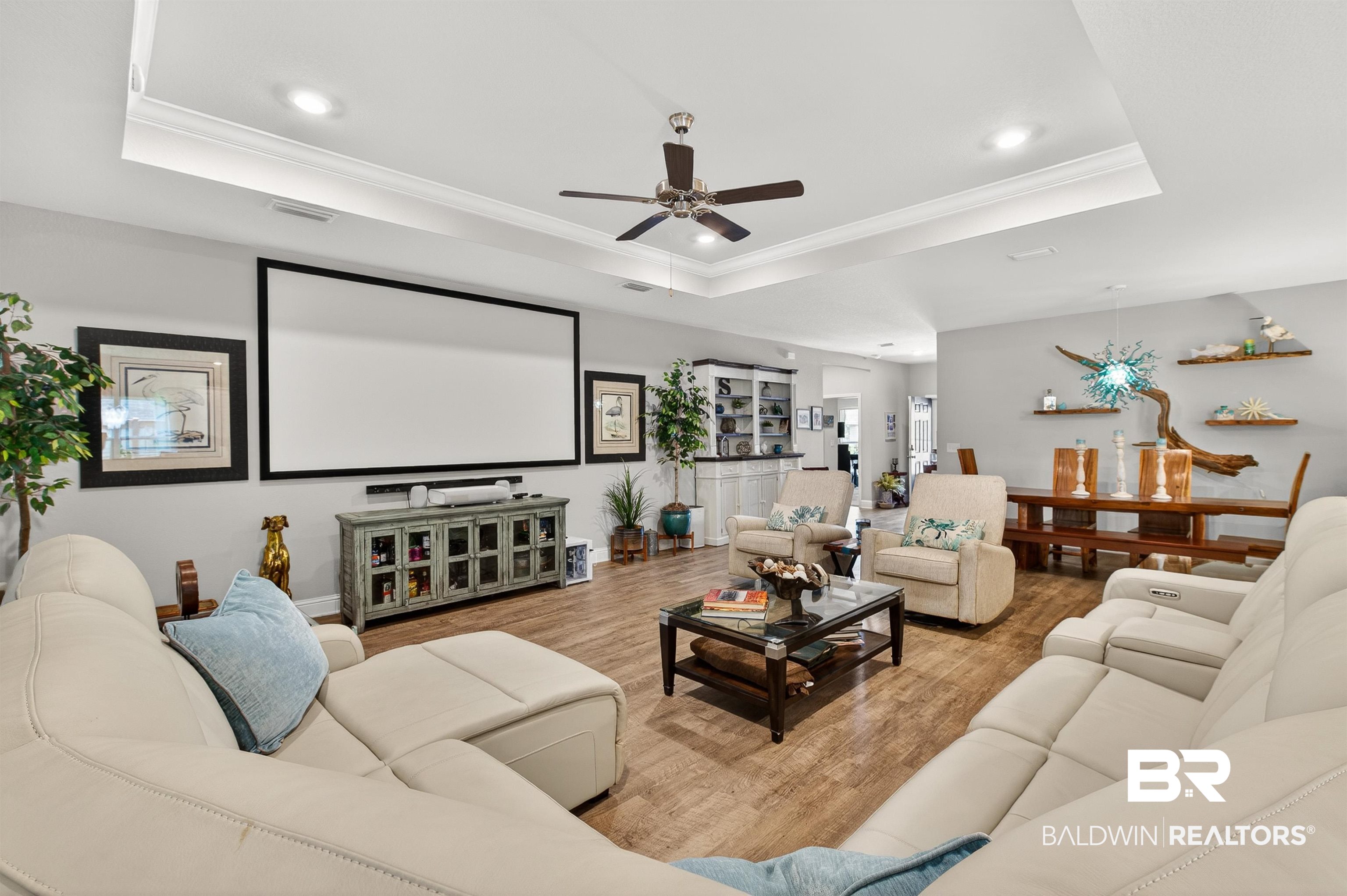 8735 Bronze Lane Foley, AL 36535 - Photo 6 of 58 Spacious living area featuring wood-finish flooring, a tray ceiling with recessed lighting and a ceiling fan, a large built-in media screen, and a console cabinet with glass-front doors