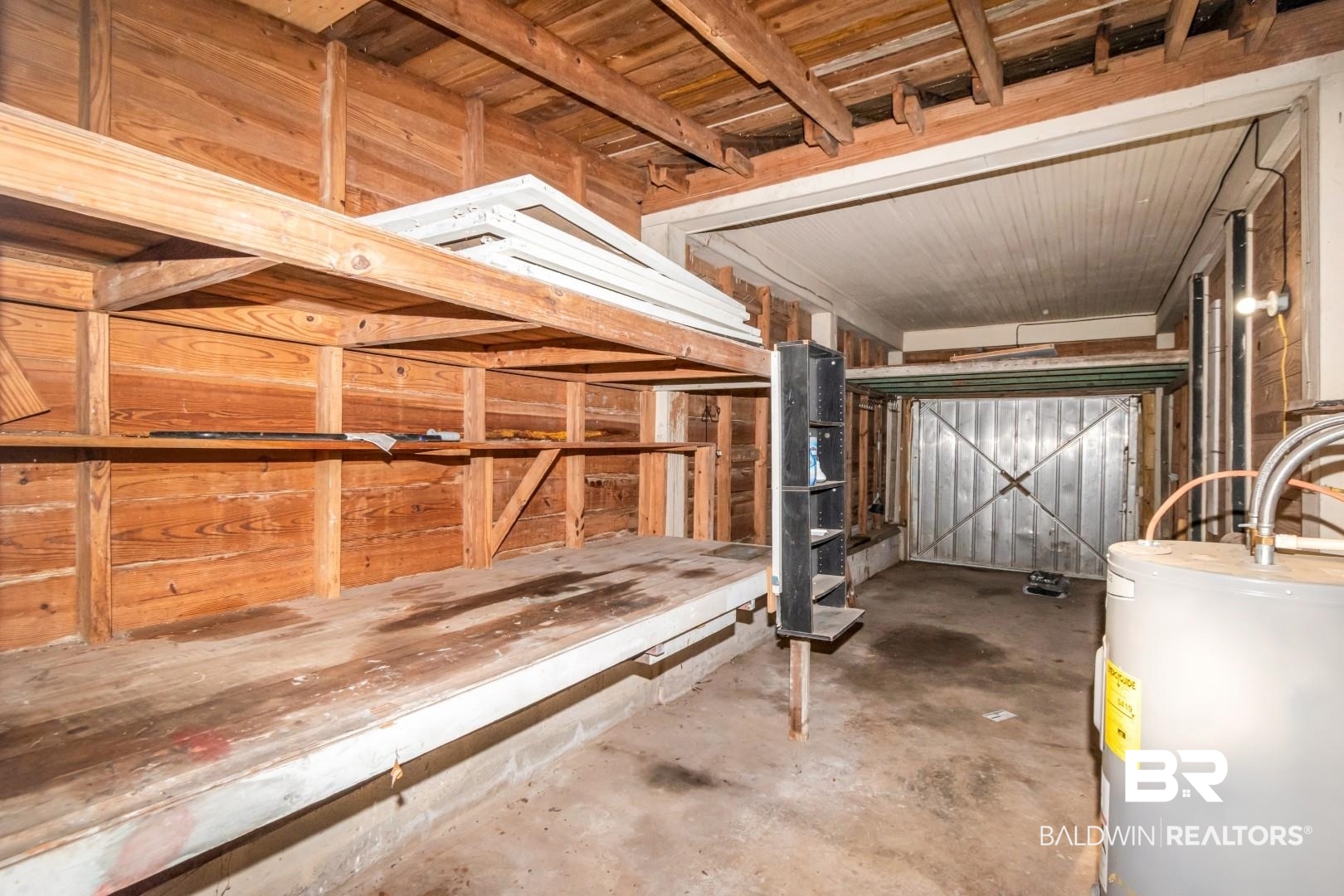 263 Border Drive East Mobile, AL 36608 - Photo 25 of 27 Garage space featuring built-in wooden shelving, a workbench, exposed wood beam ceiling, concrete flooring, and a water heater unit