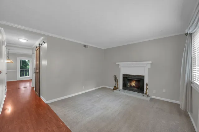 a view of an empty room with wooden floor fireplace and a window