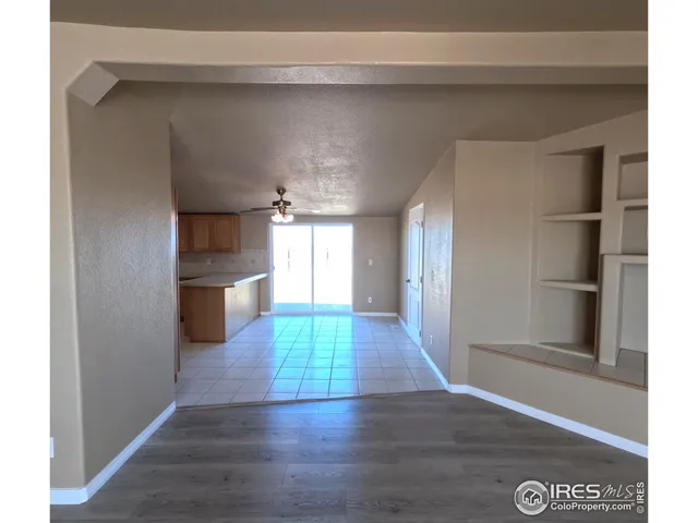 a view of a refrigerator in kitchen and an empty room with wooden floor