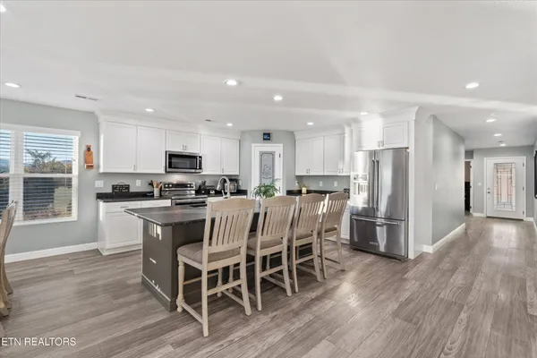 a living room with stainless steel appliances kitchen island granite countertop a table chairs and a refrigerator