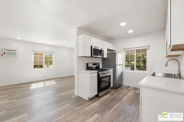 a kitchen with granite countertop a stove top oven a sink dishwasher a refrigerator and a dining table with wooden floor