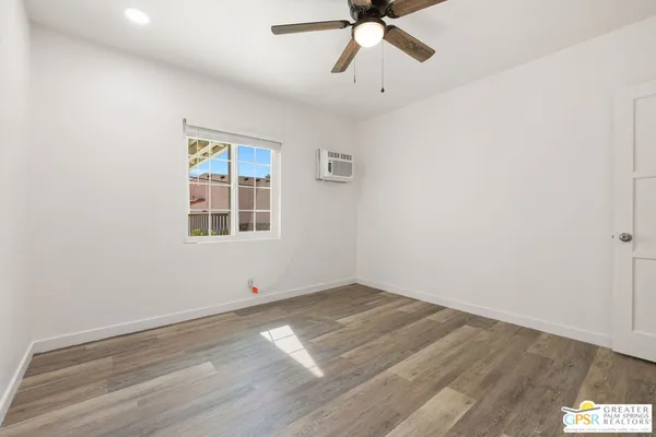 an empty room with wooden floor fan and windows