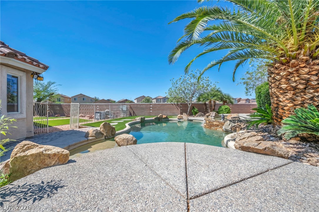 6405 North Raptor Court North Las Vegas, NV 89084 - Photo 49 of 66 An inviting backyard oasis awaits with a sparkling pool, rock features, and lush palm trees.