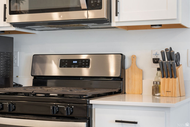 1693 Devils Gdn Lane Washington, UT 84780 - Photo 15 of 64 Stainless steel microwave with range hood, black gas range with grates, white cabinetry, and light-toned countertop