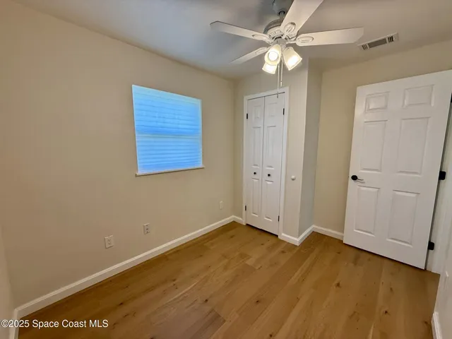 an empty room with wooden floor and fan