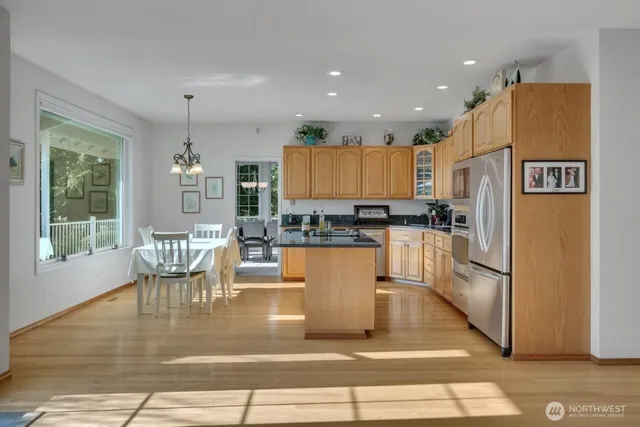 a kitchen with stainless steel appliances granite countertop a refrigerator a stove and a dining table with wooden floor