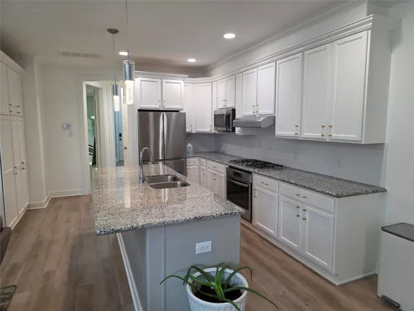 a kitchen with stainless steel appliances granite countertop a sink dishwasher a refrigerator and white cabinets with wooden floor