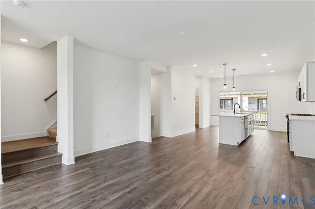 a view of an empty room and kitchen with wooden floor