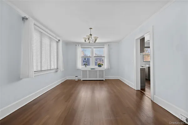 an empty room with wooden floor chandelier and windows