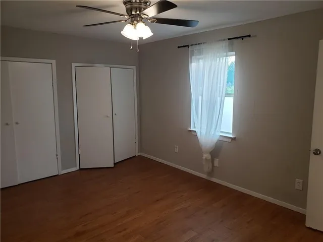 an empty room with wooden floor closet and windows