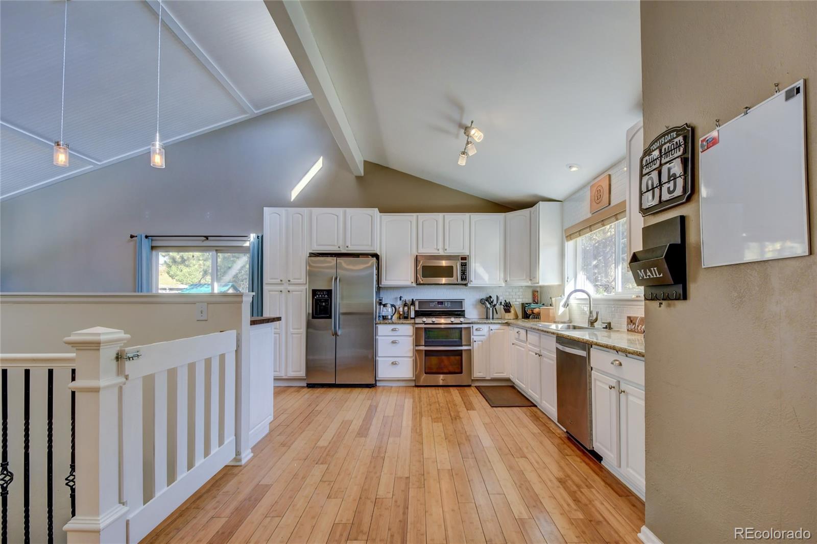 6359 Powell Road Parker, CO 80134 - Photo 5 of 38 a kitchen with stainless steel appliances a microwave a stove a sink dishwasher a refrigerator white cabinets with wooden floor