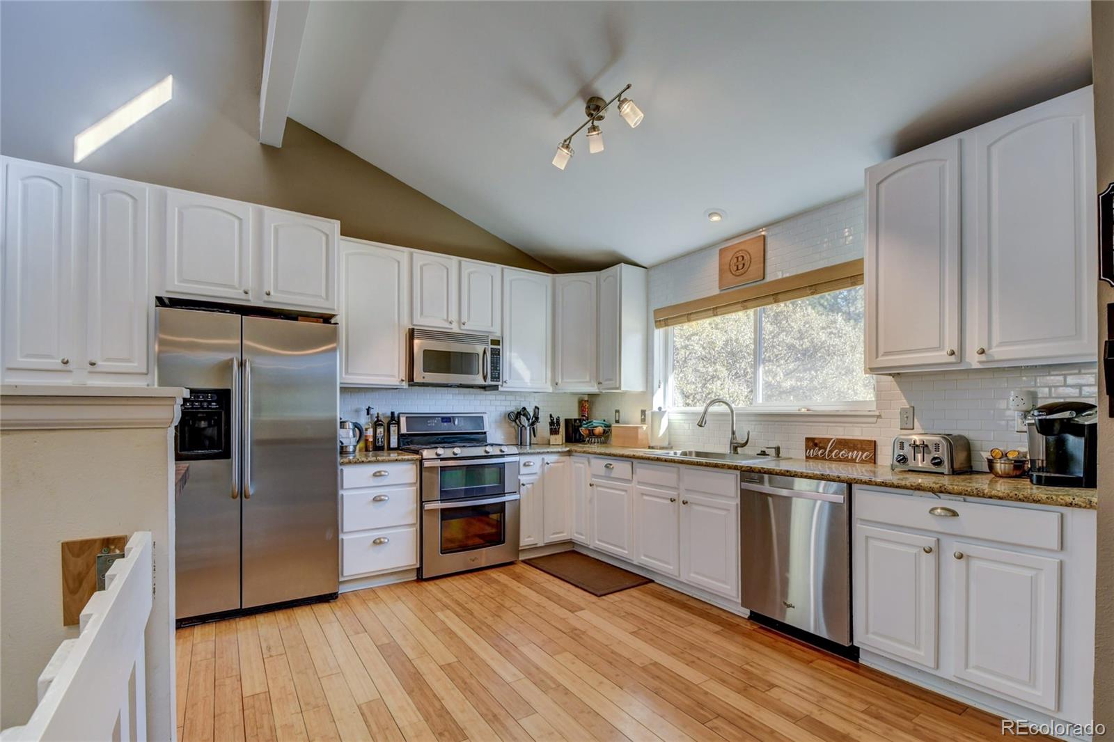 6359 Powell Road Parker, CO 80134 - Photo 6 of 38 a kitchen with stainless steel appliances granite countertop white cabinets a sink a stove a refrigerator and island with wooden floor