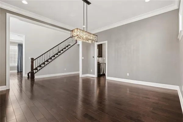 a view of an empty room with wooden floor stairs and a chandelier