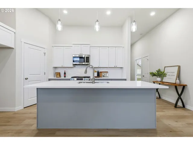 a living room with stainless steel appliances kitchen island a table chairs in it and wooden floors