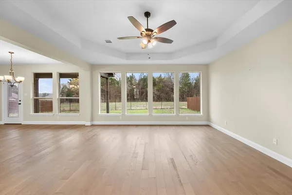 a view of an empty room with wooden floor and a ceiling fan