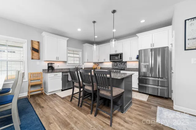 a kitchen with stainless steel appliances a refrigerator a stove a sink dishwasher a dining table and chairs cabinets with wooden floor