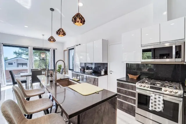 a open kitchen with stainless steel appliances granite countertop a stove a refrigerator a kitchen island a dining table and chairs with wooden floor