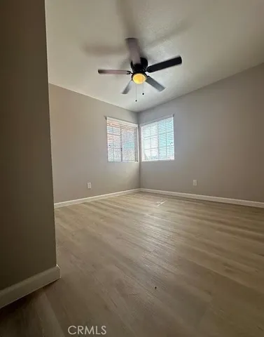 an empty room with wooden floor ceiling fan and windows