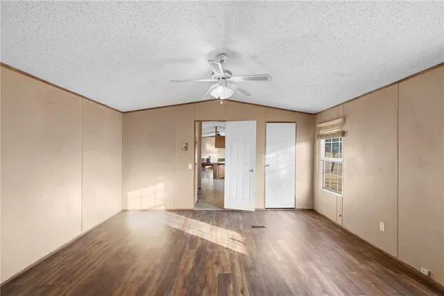 an empty room with wooden floor chandelier fan and windows
