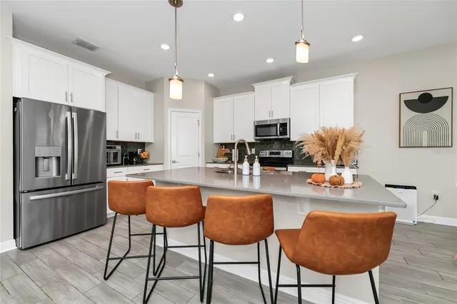 a kitchen with stainless steel appliances kitchen island granite countertop a refrigerator a stove a kitchen island a dining table and chairs with wooden floor