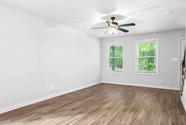 an empty room with wooden floor fan and windows