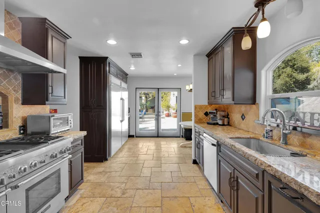 a large kitchen with stainless steel appliances granite countertop a stove top oven a sink dishwasher a dining table and chairs with wooden floor